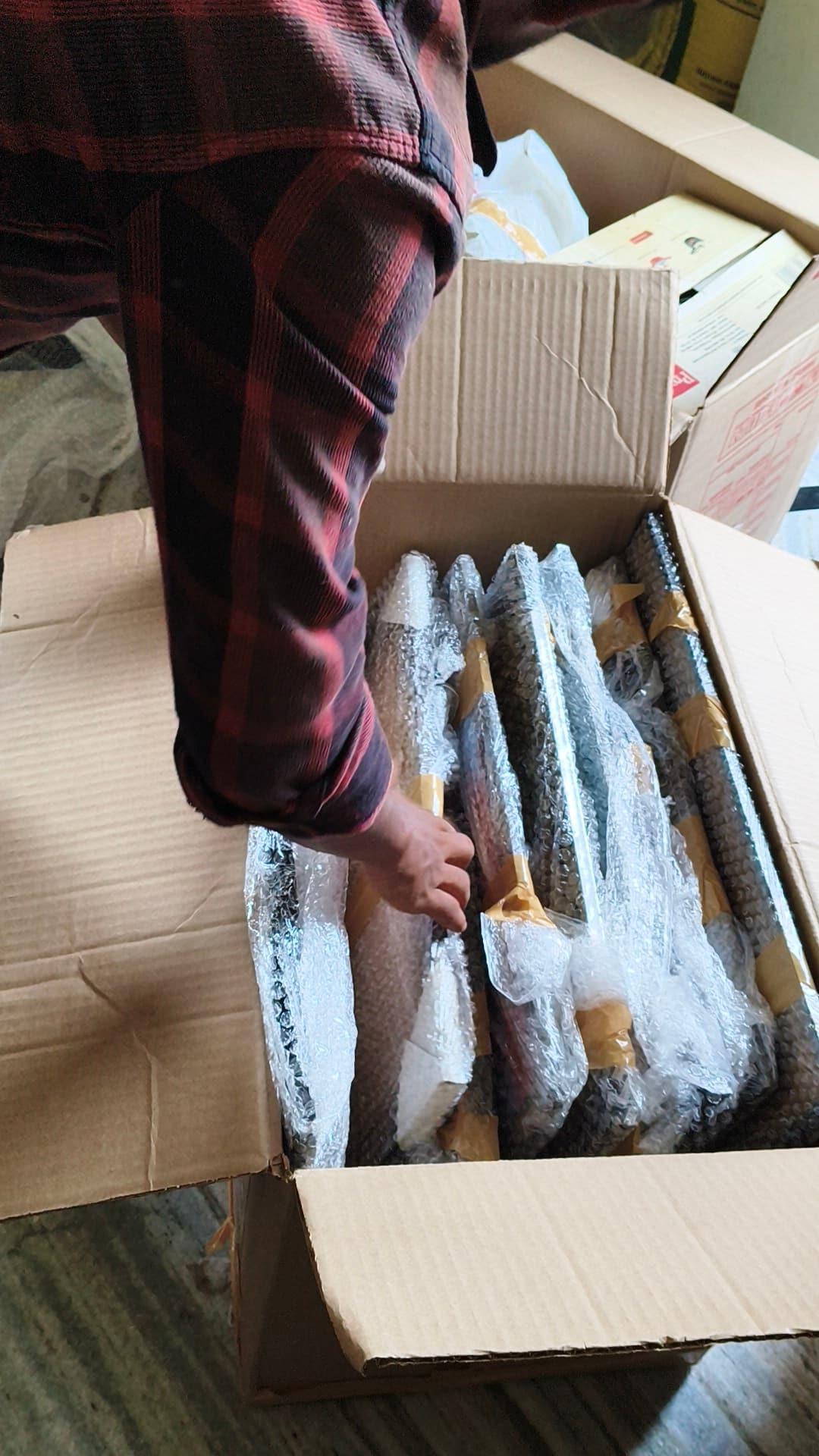 A packer placing individually bubble-wrapped rods into a cardboard carton during a household pack