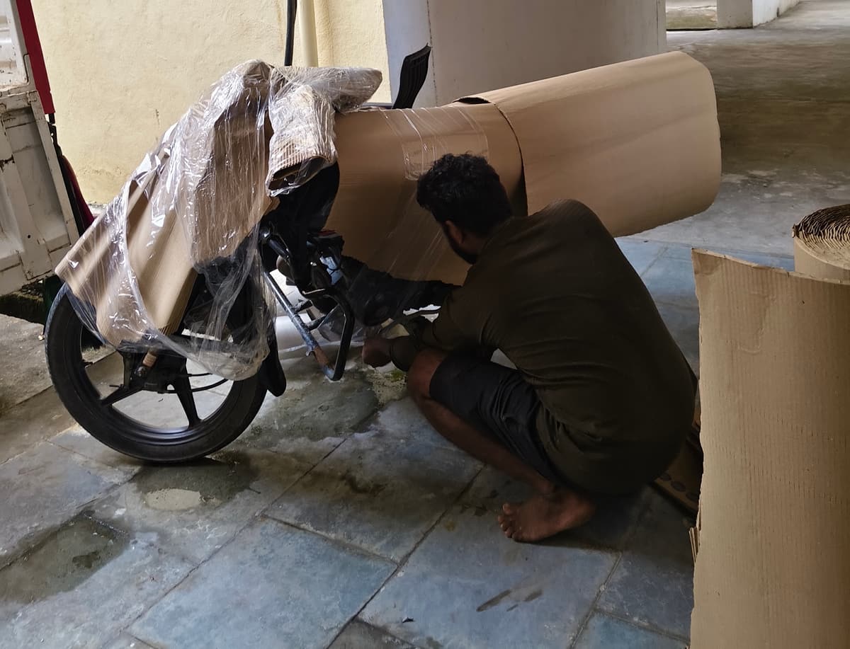 A Dwaraka worker wrapping a motorcycle in corrugated cardboard sheeting before transport