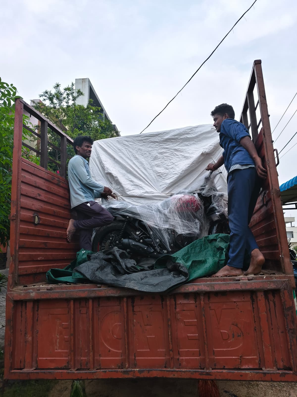 A motorcycle wrapped in protective film secured inside a truck bed with two crew members alongside