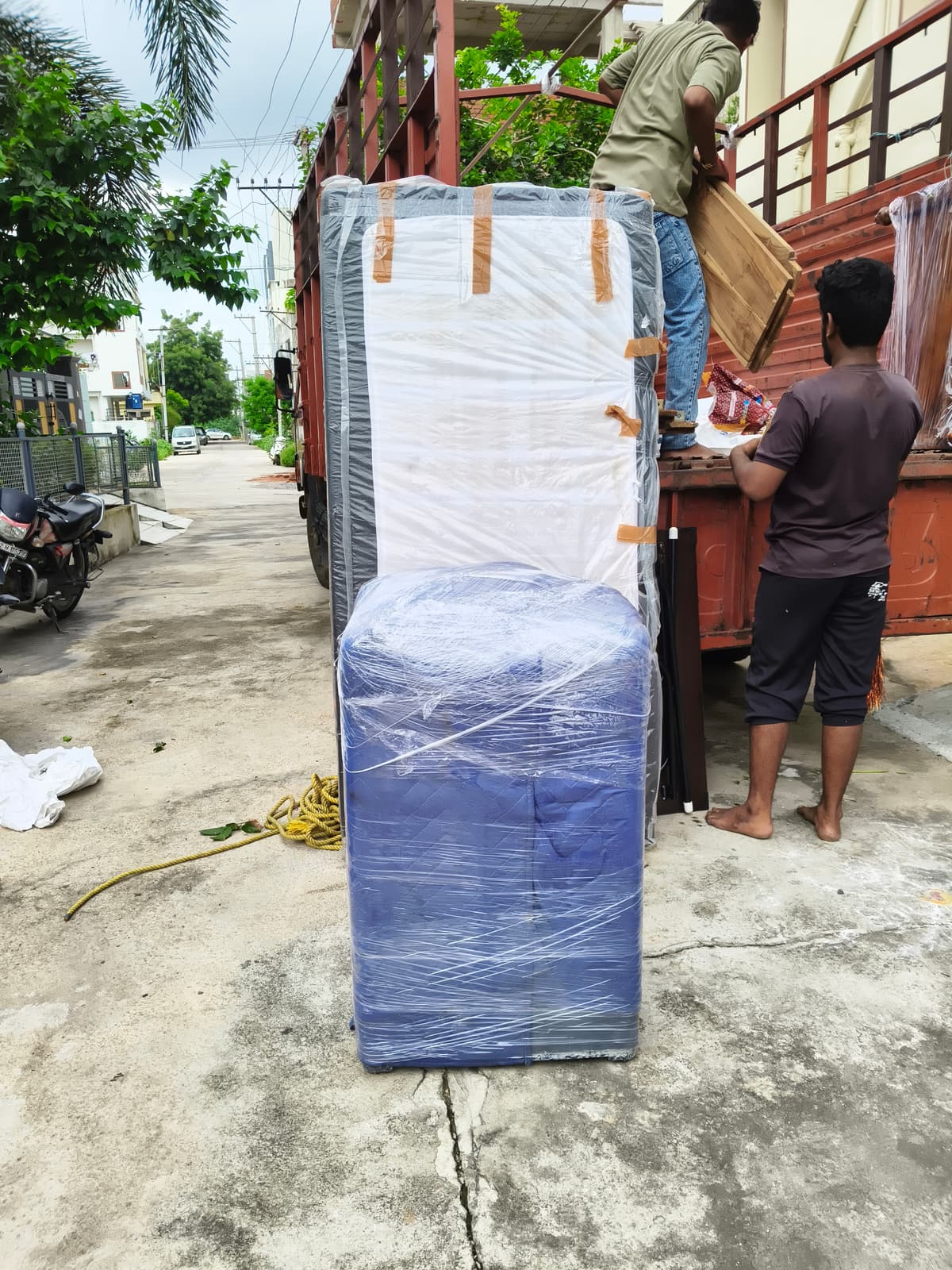 A padded and wrapped washing machine and mattress on a street as movers load furniture into a truck